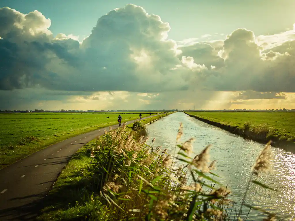 Fietspad door het groene polderlandschap van het Eiland van Schalkwijk, met een waterkanaal en dramatische wolkenlucht in warm middaglicht.
