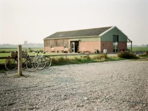 Grindparkeerplaats bij een rustiek boerderijrestaurant in het Utrechtse polderlandschap, fietsen tegen een verweerde houten paal.